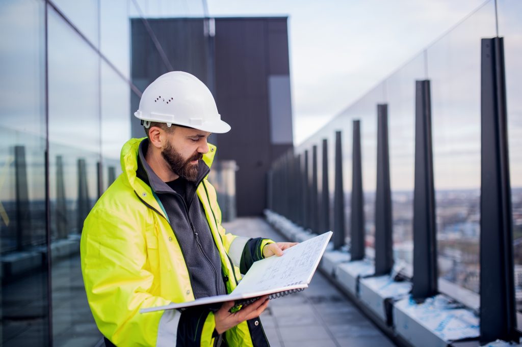 Man engineer standing on construction site holding blueprints